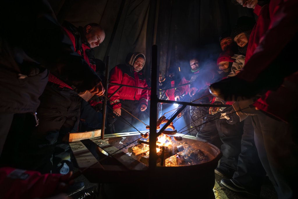 Group of people grilling sausages in a hut.
